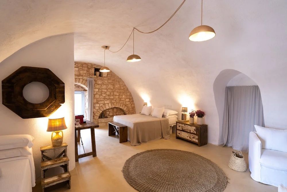 Gewölbtes Hotelzimmer mit Natursteinwand, Doppelbett und warmem Licht.