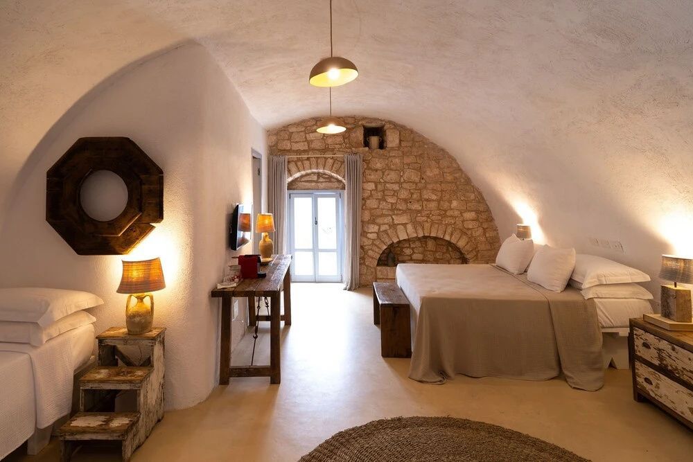 Schlafbereich unter einem Steingewölbe mit Doppelbett und Holztisch.