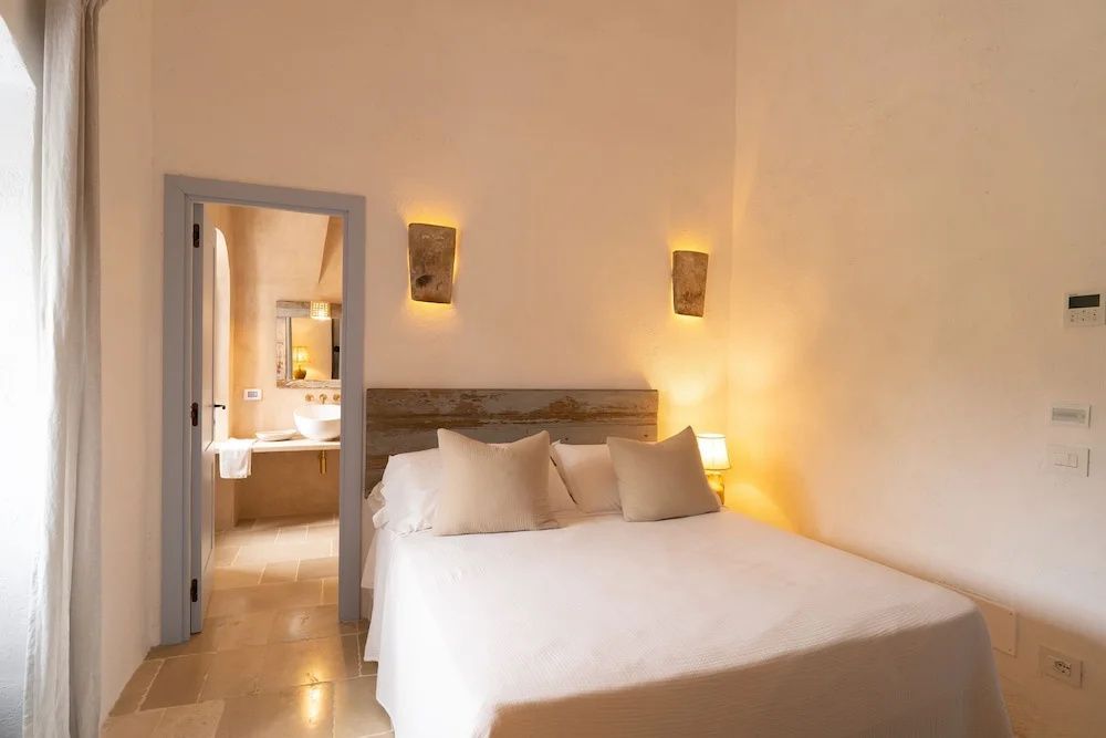 Helles Schlafzimmer mit Doppelbett und Blick in das angrenzende Badezimmer.