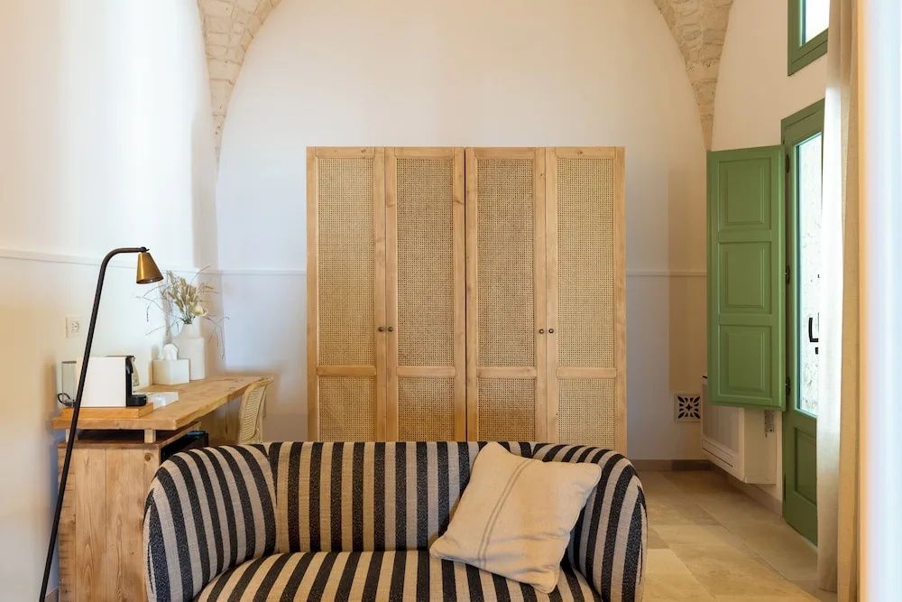 Gestreiftes Sofa im Vordergrund und ein dreitüriger Schrank aus Holz in einem Raum mit Gewölbedecke.