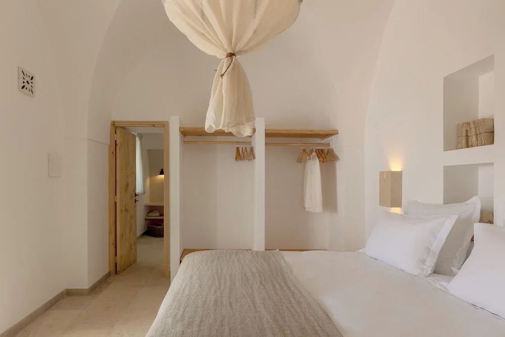 Heller Schlafbereich mit großem Bett, offener Garderobe und hängendem Stoffschirm an der Decke.