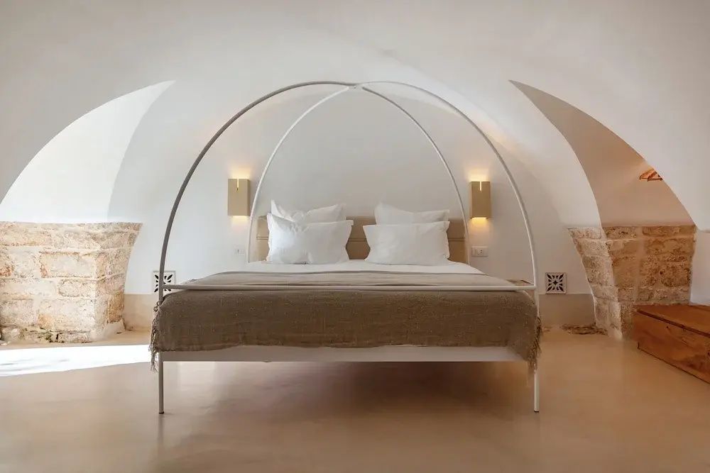 Doppelbett mit Metallbaldachin unter einem beigefarbenen Kreuzgewölbe.