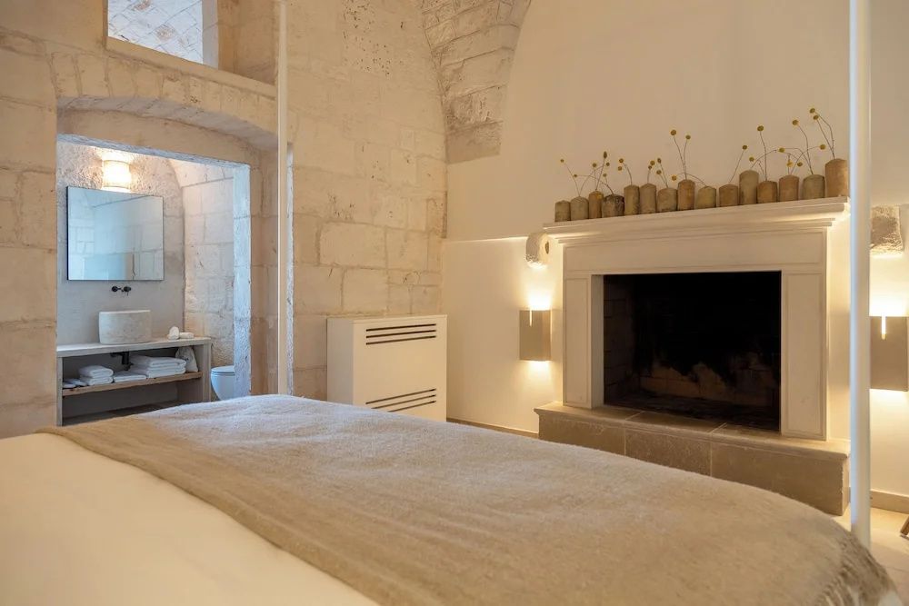 Helles Schlafzimmer mit gewölbter Steinwand, einem Kamin und Zugang zum Badezimmer.