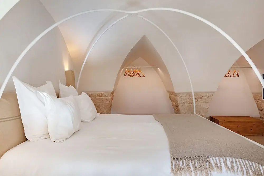 Doppelbett mit weißem Himmelbettgestell vor einer spitzzulaufenden Wandnische mit Kleiderbügeln.
