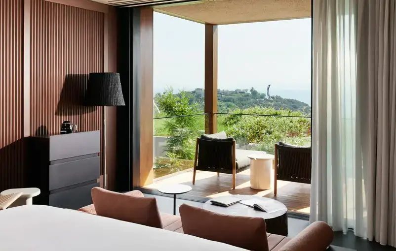 Blick vom Hotelzimmer auf die Terrasse mit Sitzmöbeln und die begrünte Landschaft.