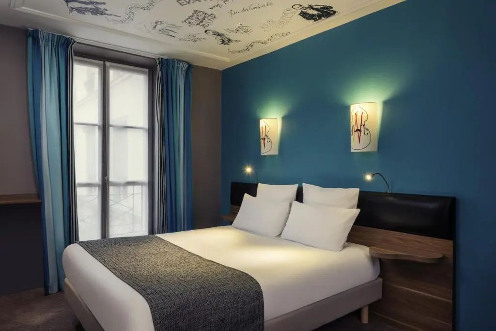 Doppelbett mit weißer Bettwäsche vor einer blauen Wand und Fenster mit blauen Vorhängen.