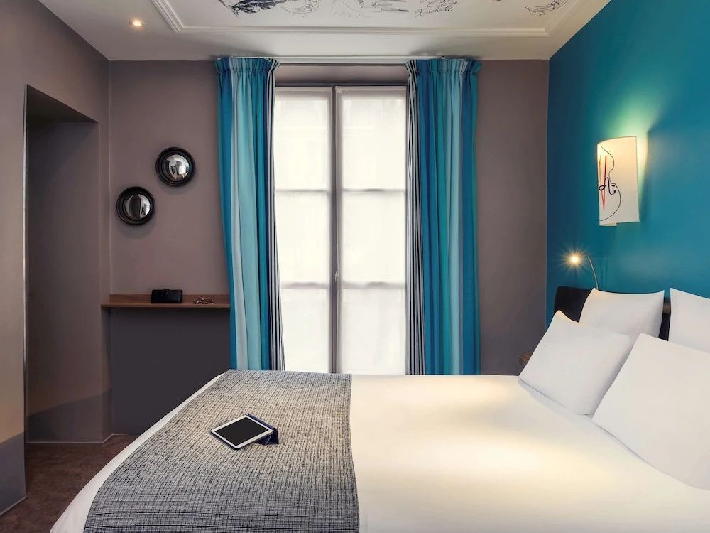 Doppelbett im Hotelzimmer neben einem Fenster mit blau gestreiften Vorhängen.