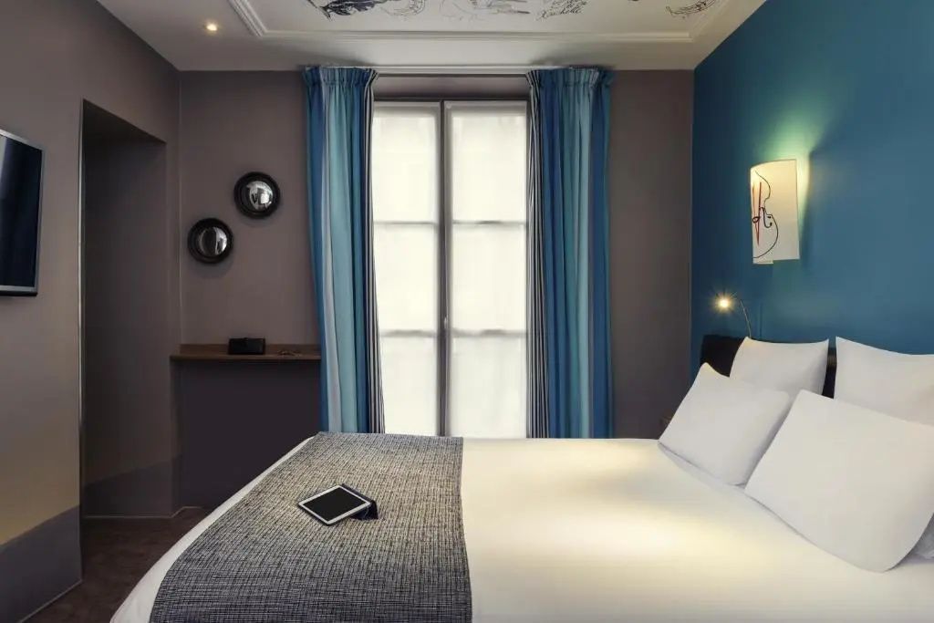 Doppelbett in einem Hotelzimmer mit Fenster, blauen Vorhängen und blau gestrichener Wand.