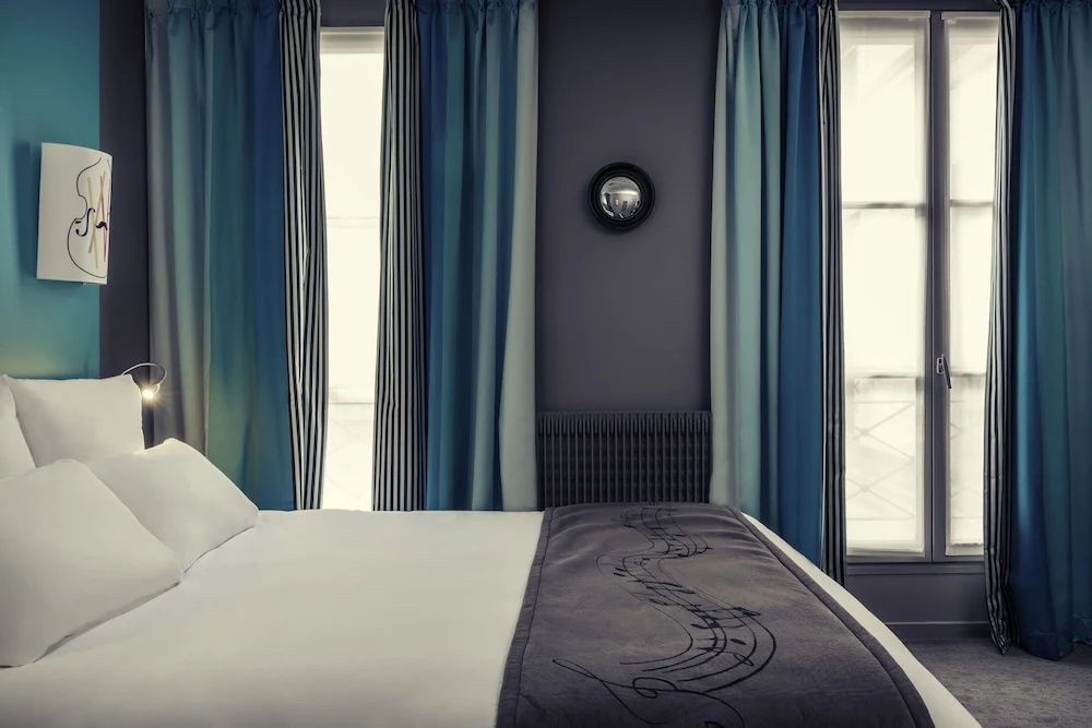 Bettende mit bestickter Tagesdecke vor Fenstern mit blau gestreiften Vorhängen.