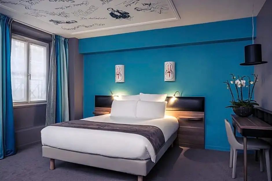 Hotelzimmer mit großem Doppelbett, blauem Wandakzent und verzierter Zimmerdecke.