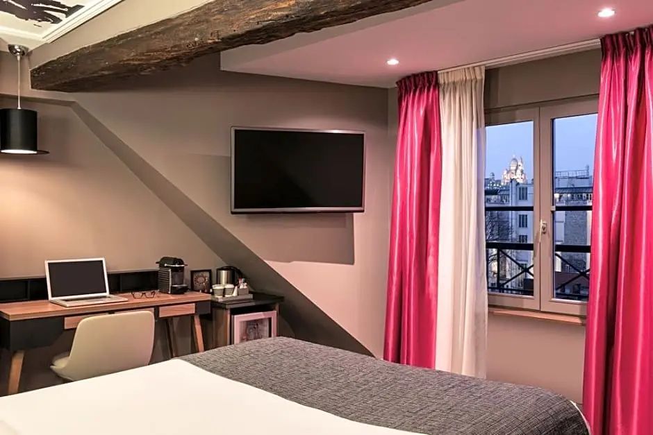 Hotelzimmer mit Dachschräge, Holzbalken, Flachbild TV, Schreibtisch und Fensterblick.