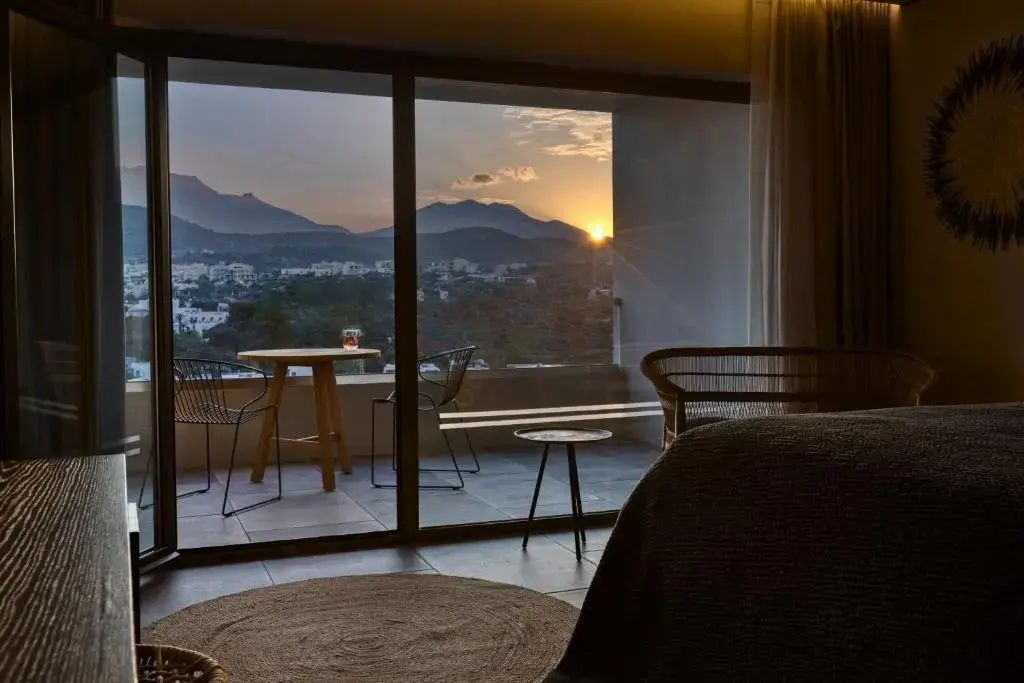 Blick vom Zimmer auf Balkon und Berge bei Sonnenuntergang durch große Glasfront.