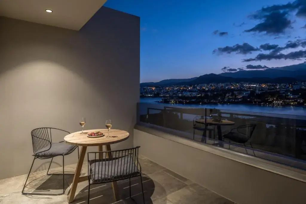 Balkon bei Dämmerung mit Holztisch, zwei Weingläsern und Blick auf die beleuchtete Stadt.
