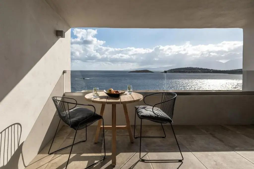 Balkon mit Holztisch und zwei Stühlen mit freiem Blick auf das blaue Meer und Inseln.
