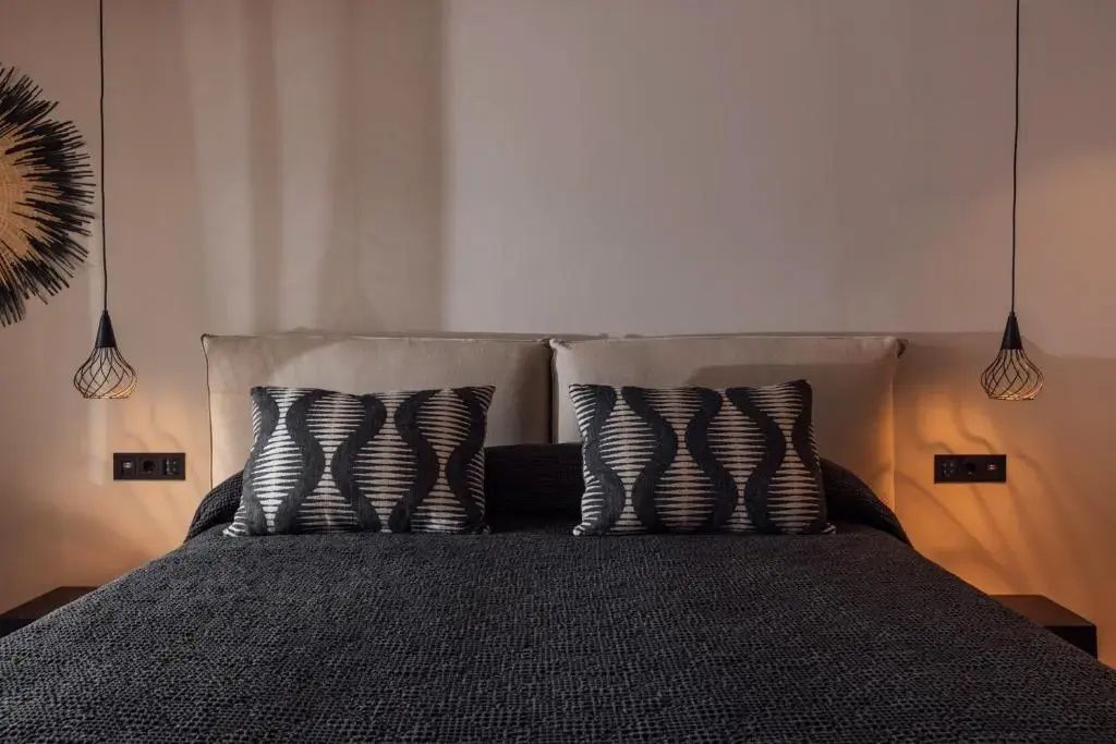 Doppelbett mit dunkelgrauer Decke und zwei gemusterten Kissen vor hellem Kopfteil.