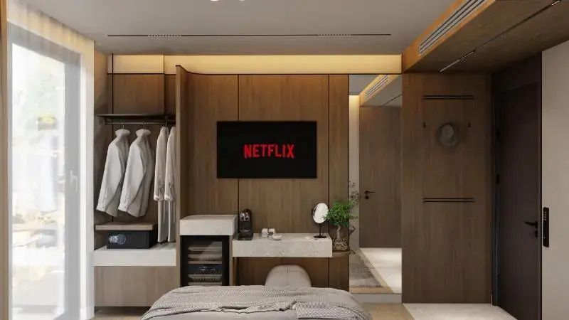 Holzverkleideter Wandbereich im Hotelzimmer mit Fernseher, Minibar und Durchgang zum Flur.