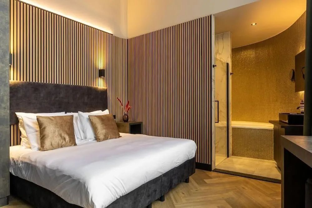 Doppelbett mit weißer Bettwäsche und braunen Kissen vor einer Wand mit Holzlamellen.