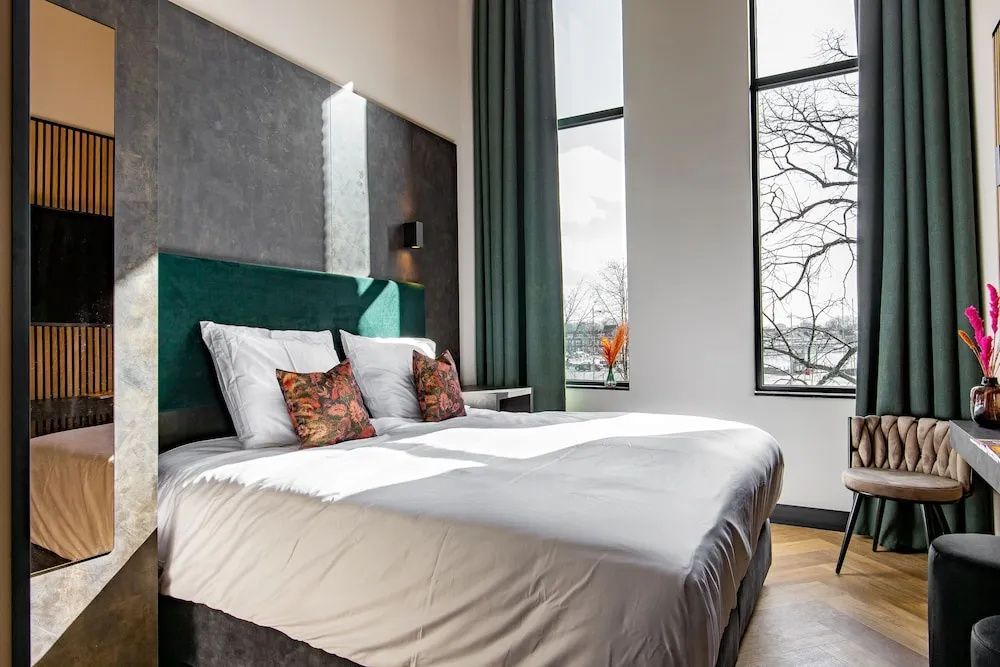 Doppelbett im geräumigen Zimmer mit hohen Fenstern und Blick ins Grüne.
