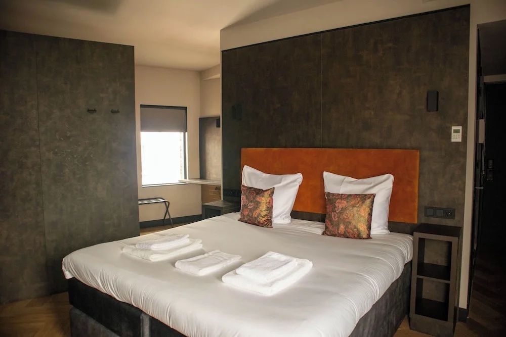 Doppelbett mit weißer Bettwäsche, orangefarbenem Kopfteil und gemusterten Kissen im Hotelzimmer.
