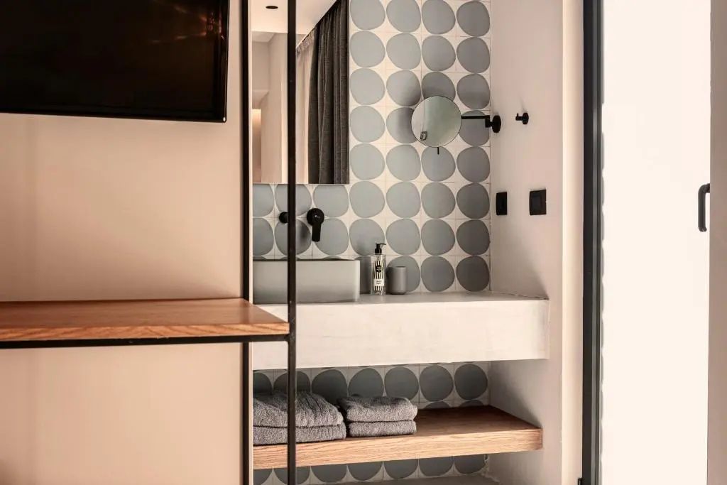 Modernes Badezimmer mit grau gepunkteten Wandfliesen, Waschtisch und Holzablage mit Handtüchern.