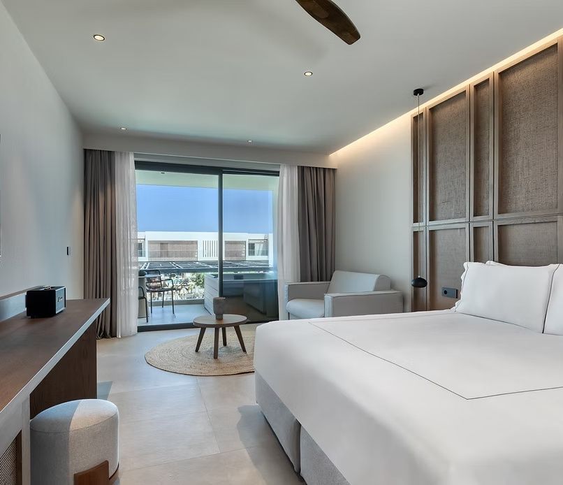 Lichtdurchflutete Suite mit großem Doppelbett, Sitzecke und Balkon mit Sitzgelegenheit.