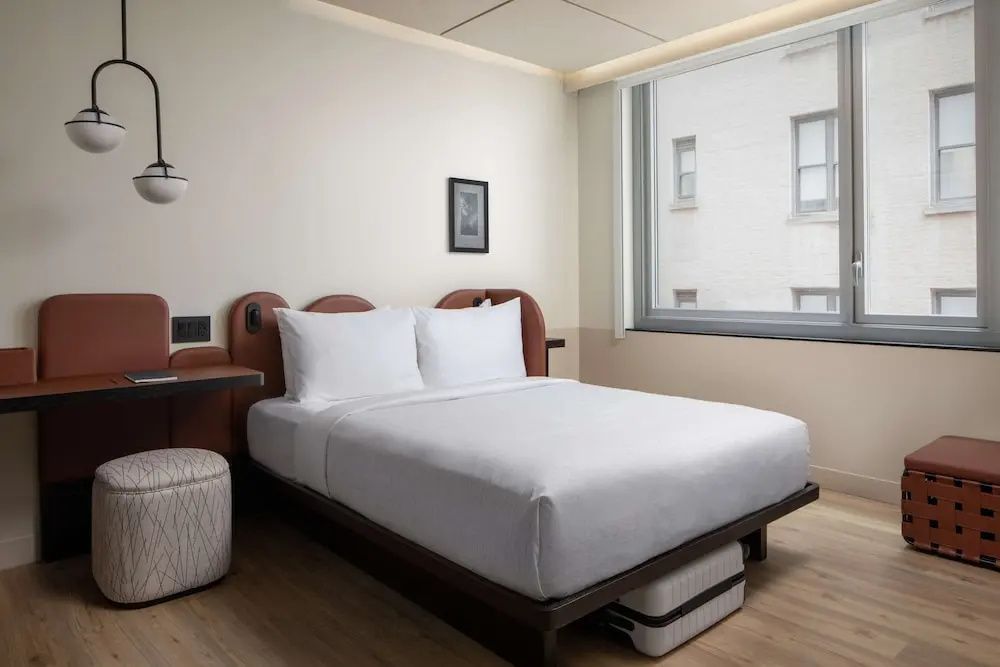 Hotelzimmer mit Doppelbett, Koffer unter der Liegefläche und Blick aus dem Fenster.