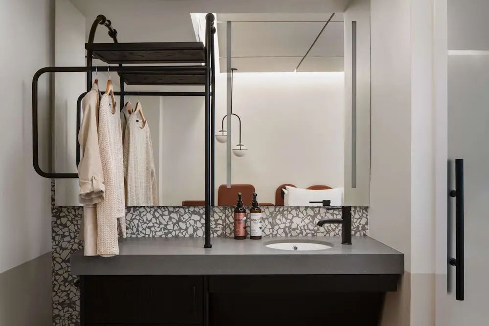 Waschbereich mit Spiegel, rechteckiger Ablage, Waschbecken und offener Garderobe.