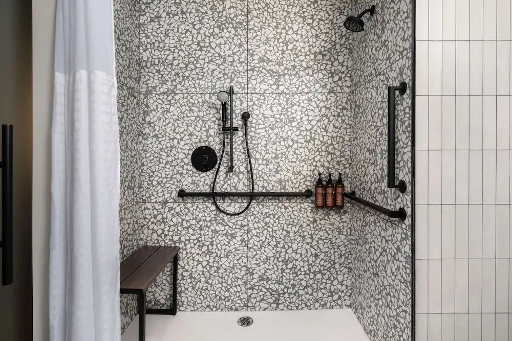 Geflieste Dusche mit gepunktetem Muster, schwarzen Armaturen und einer kleinen Sitzbank.