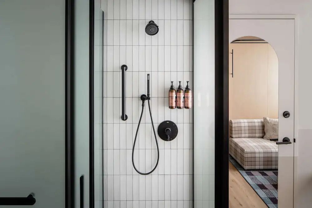 Begehbare Dusche mit weißen Fliesen, schwarzen Armaturen und Seifenspendern an der Wand.