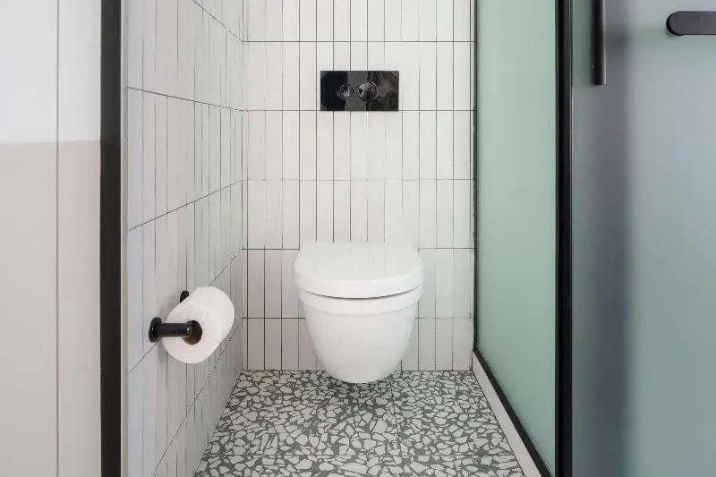 Moderne Toilette mit vertikalen weißen Wandfliesen und gepunktetem Mosaikboden.