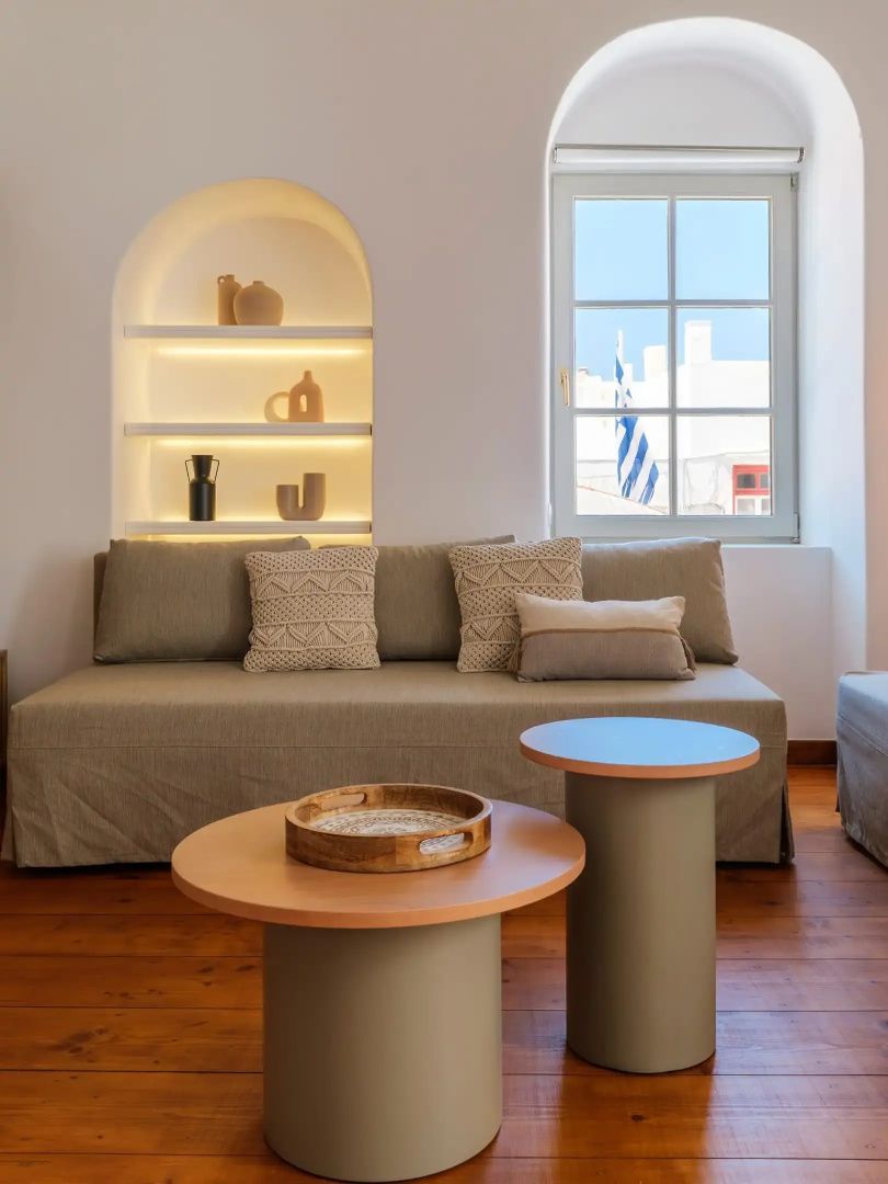 Ein Sitzbereich mit beige gepolstertem Sofa, zwei runden Couchtischen und beleuchteter Nische.