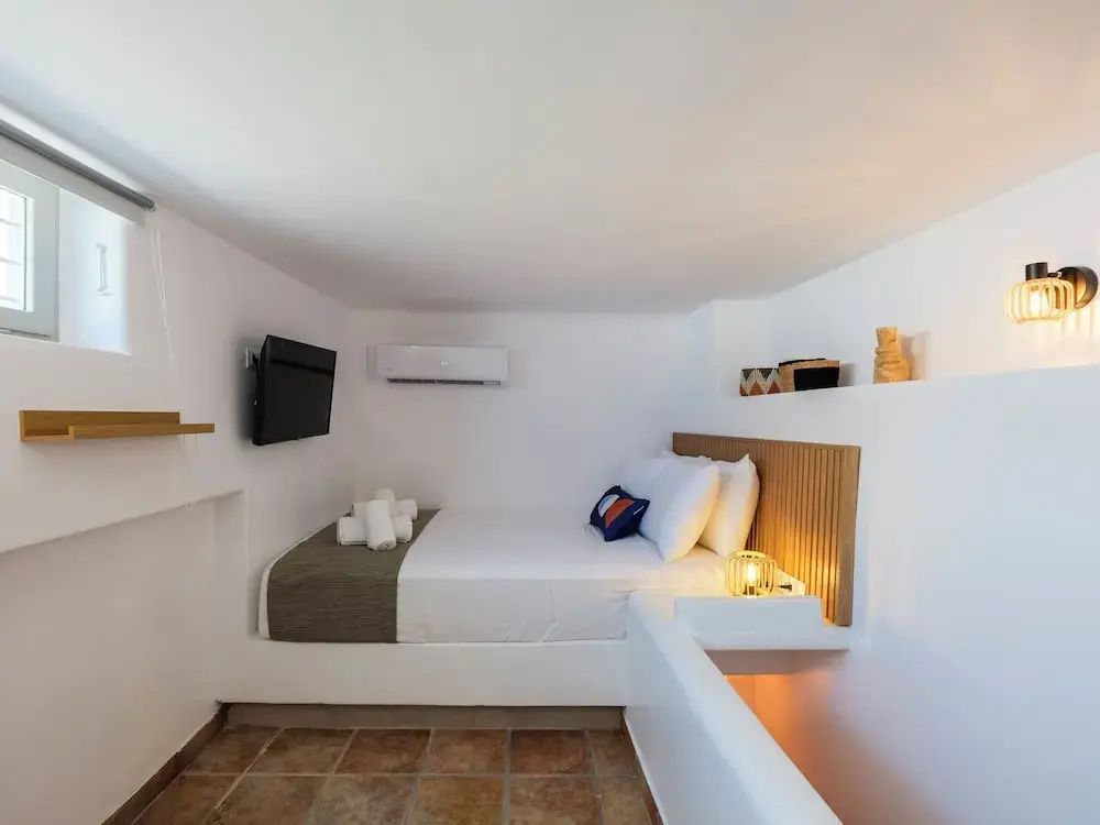 Weiß gestalteter Schlafbereich mit Doppelbett, Wand-TV und Fliesenboden.