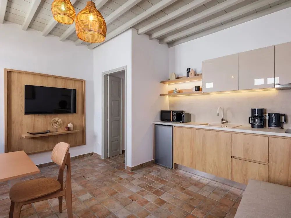 Blick in den Wohnraum mit Küchenzeile, Flachbildfernseher an Holzverkleidung und Essbereich.