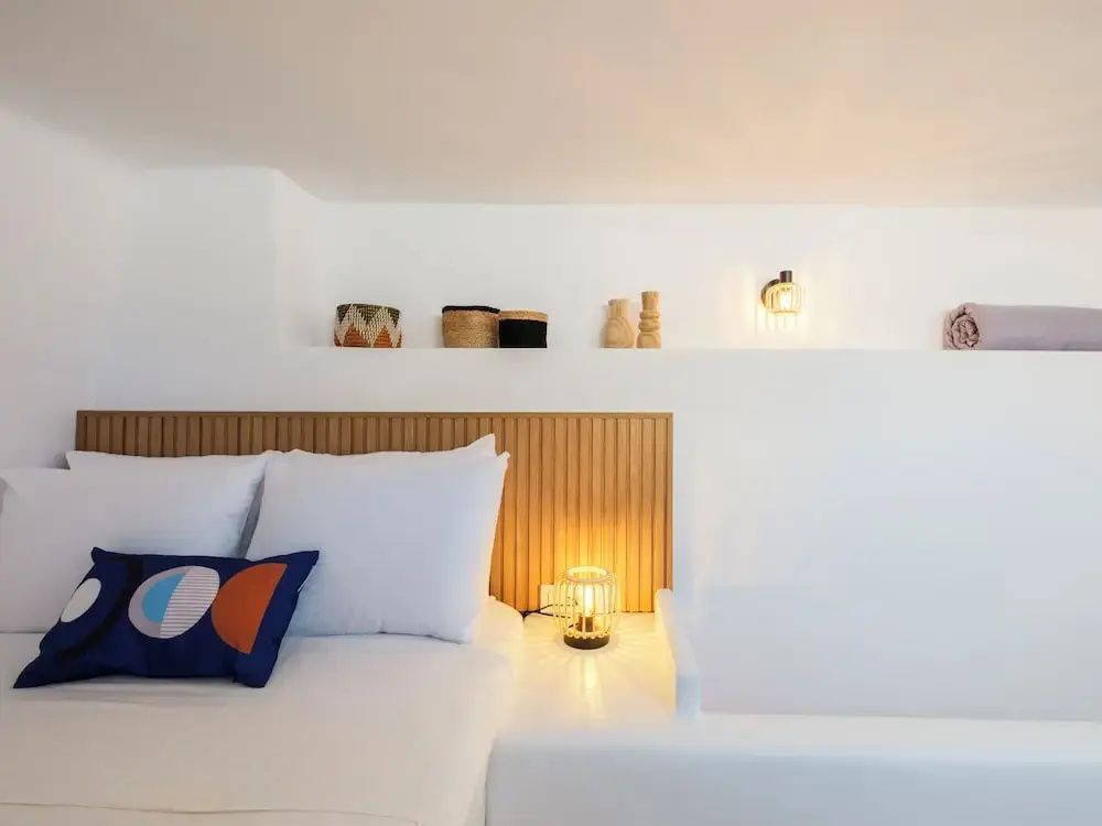 Bett mit Holzkopfteil, Nachttischlampe und dekorativen Körben in einer Wandnische.