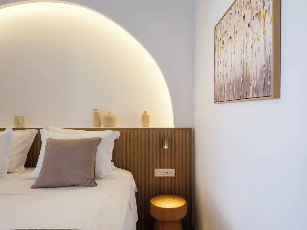 Bett mit Holzverkleidung, beleuchteter Rundbogennische und hölzernem Hocker.