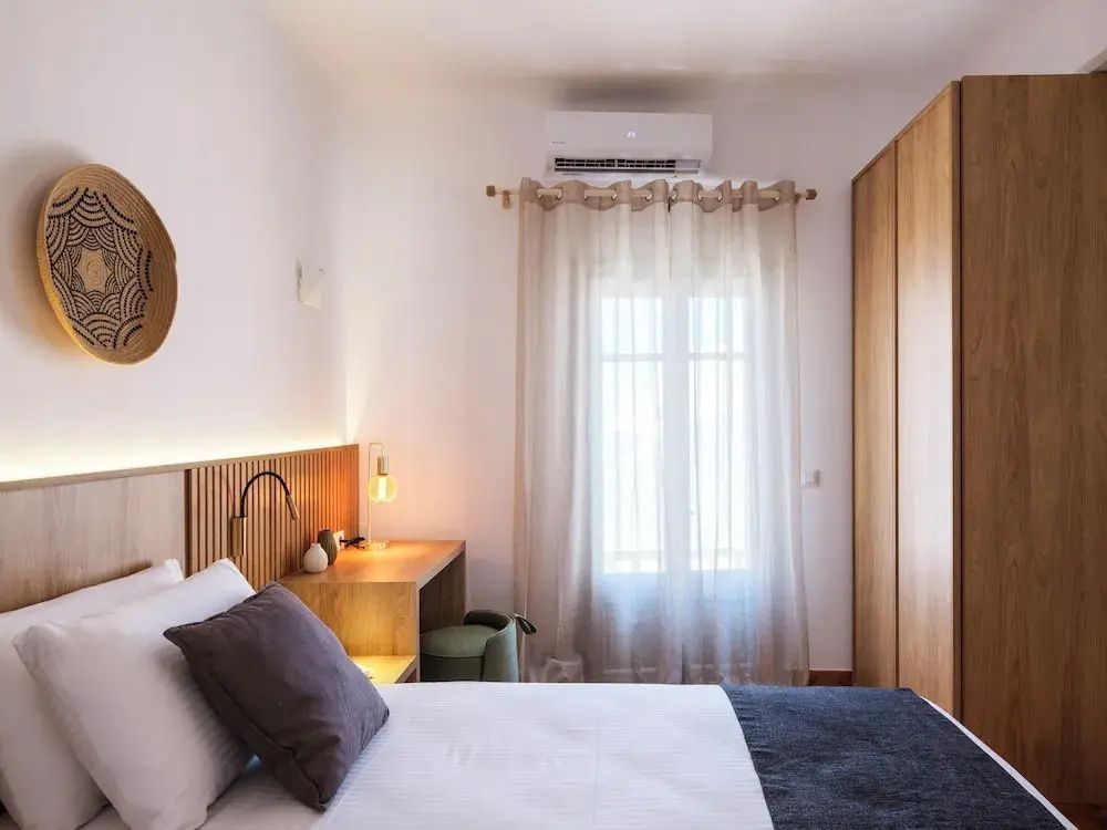 Schlafzimmer mit großem Holzkleiderschrank, Schreibtisch und hellem Vorhang.