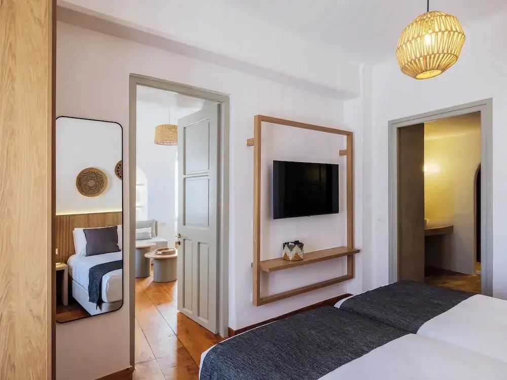 Schlafzimmer mit Fernseher auf Holzrahmen und Blick durch die Tür in den Wohnbereich.