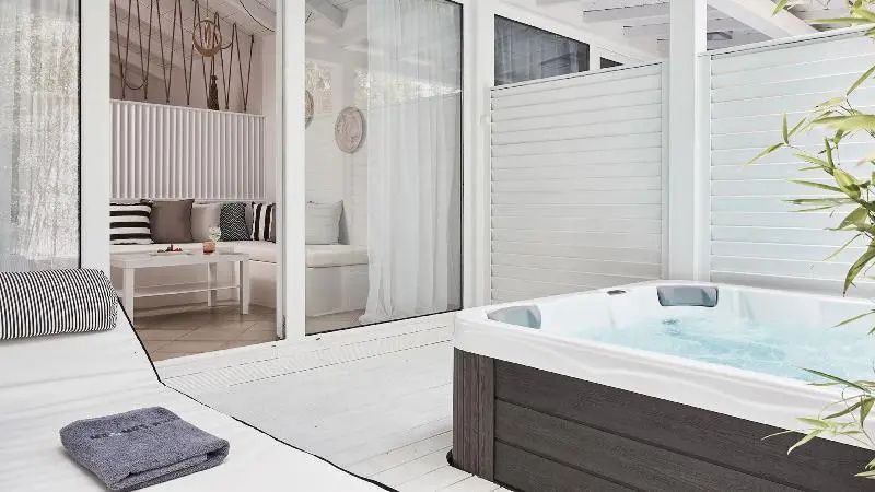 Whirlpool auf einer Holzterrasse vor gläsernen Schiebetüren zum Wohnbereich.