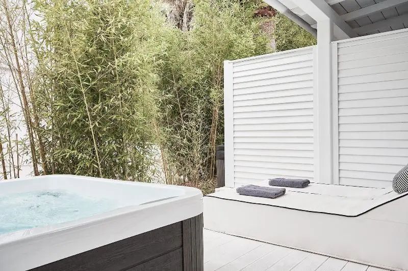 Whirlpool auf einer weißen Holzterrasse umgeben von grünen Bambuspflanzen.