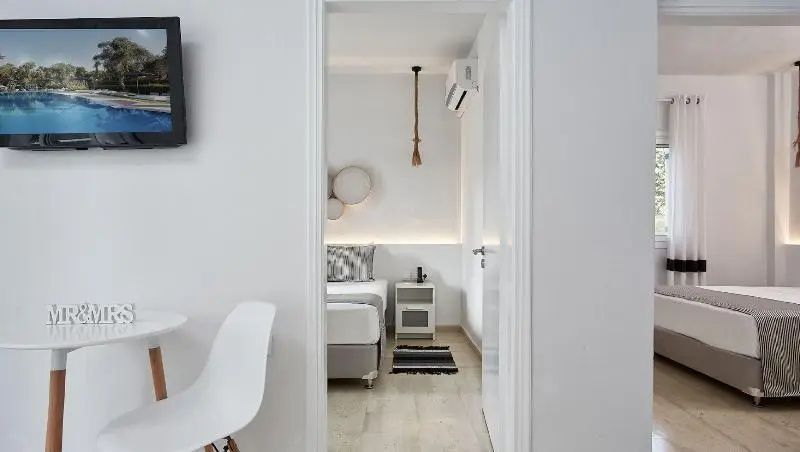 Blick durch einen Türrahmen in ein weißes Zimmer mit Bett und kleiner Kommode.
