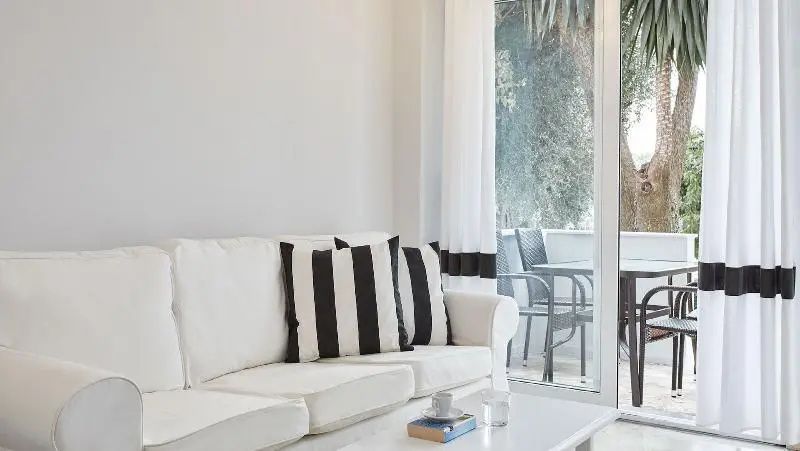 Weißes Sofa mit gestreiften Kissen neben einer geöffneten Balkontür.