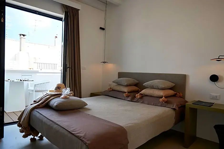 Helles Hotelzimmer mit Doppelbett, beigen Kissen und Balkontür ins Freie.