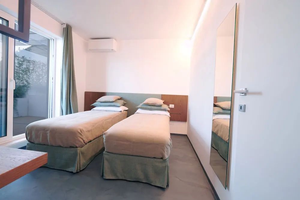 Schlichtes Hotelzimmer mit zwei Einzelbetten, Vorhängen und Wandspiegel.