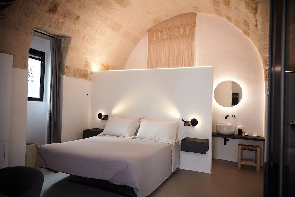 Doppelbett in einem Hotelzimmer mit Steingewölbe, Wandleuchten und offenem Badbereich.