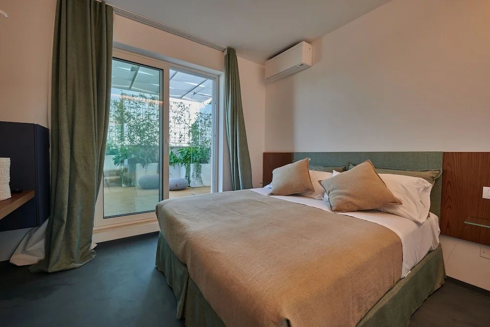 Modernes Hotelzimmer mit Doppelbett und Zugang zu einer bepflanzten Terrasse.