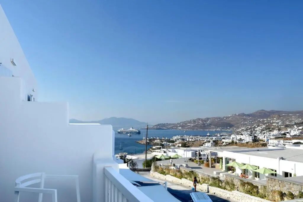 Aussicht von der Terrasse auf weiße Häuser, das Meer und ein Kreuzfahrtschiff.