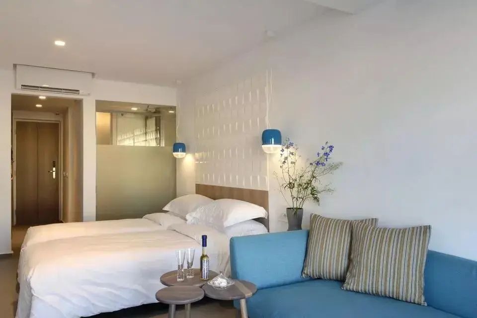 Helles Hotelzimmer mit Doppelbett, blauem Sofa, kleinen Beistelltischen und weißer Wand.