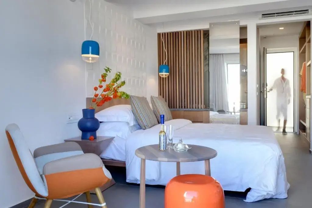 Helles Hotelzimmer mit Doppelbett, Sitzgelegenheit, kleinem Tisch und blauen Hängelampen.