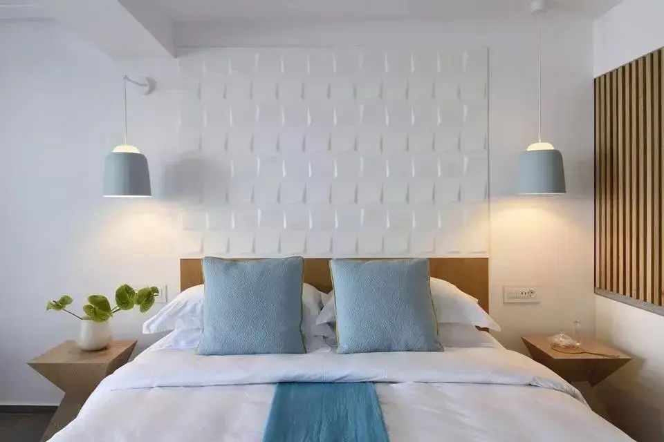 Doppelbett mit weißen Kissen, blauen Akzenten und strukturierter Wandgestaltung.