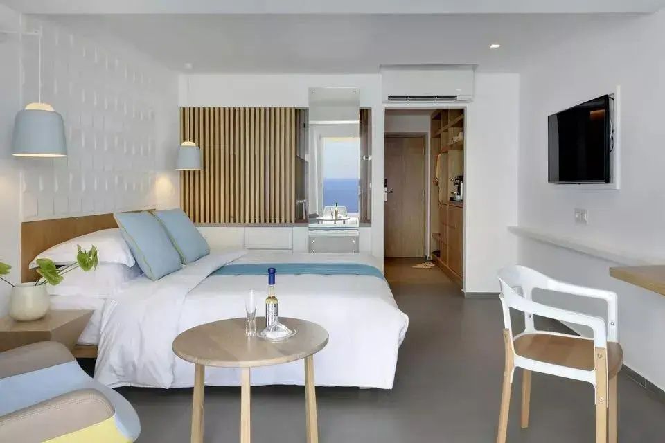 Helles Hotelzimmer mit Doppelbett, kleinem Holztisch und Blick auf das Meer.
